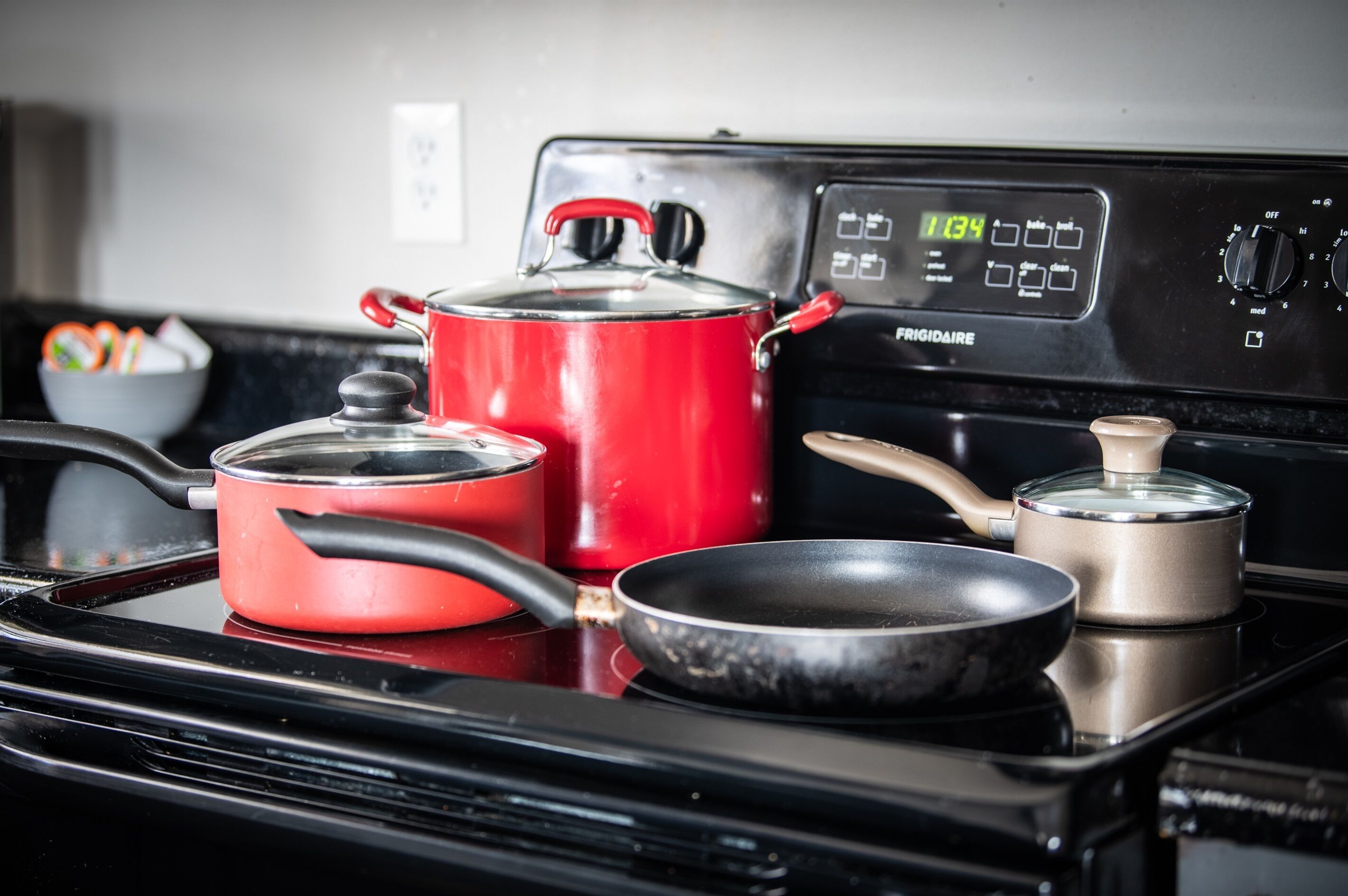 A kitchen with a red pot, a frying pan, and a smaller pot on a black stove.