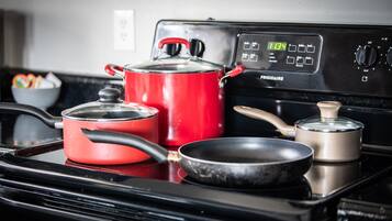 A kitchen with a red pot, a frying pan, and a smaller pot on a black stove.