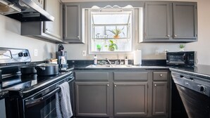 Una cocina con gabinetes grises, una estufa negra, un microondas y una ventana con plantas.