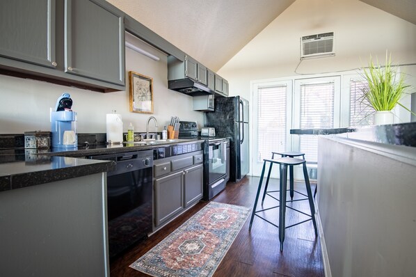 A modern kitchen with dark cabinets, a built-in oven, and a coffee maker.