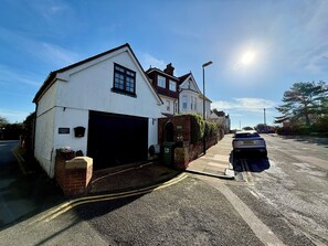 Une maison à deux étages avec un garage, une allée pavée et une voiture garée.