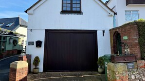 Een wit gebouw met een donkerbruine garageklep, een klein raam en een bord met de tekst 'Holywell Stays Sea View'.