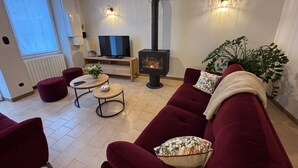 Een woonkamer met een rode bank, een televisie, een open haard en een potplant.