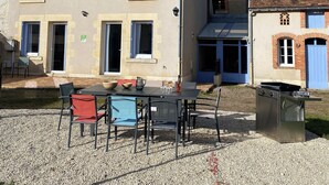 Een tweelaags huis met een patio, compleet met een tafel, stoelen, een barbecue en een kleine tuin.