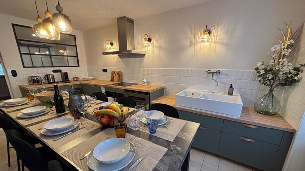Een moderne keuken met een eethoek, met een groot schiereiland, een spoelbak, een inbouwoven en een afzuigkap.