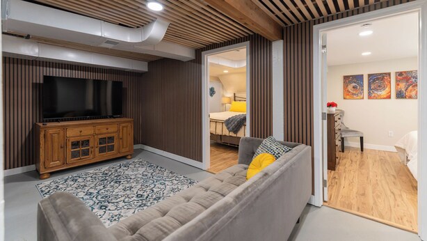 A modern living room with a wooden ceiling, a large flat-screen TV, a sofa, and a patterned rug. - Spacious, Central Location 4-bedroom, King Beds - Walk to Dining, Brewery, Park (Spokane)