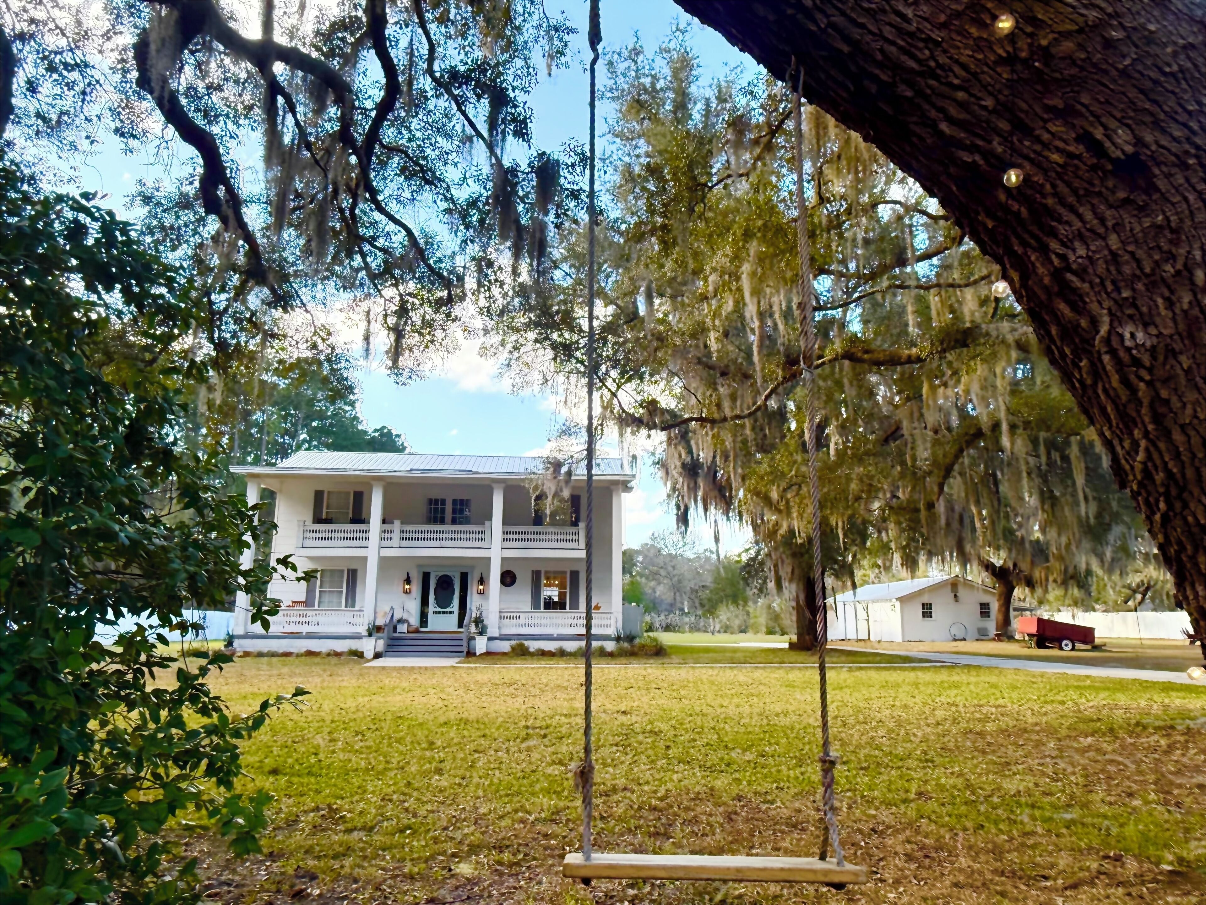 A white colonial-style house with a front porch, surrounded by a grassy lawn and trees with Spanish moss.