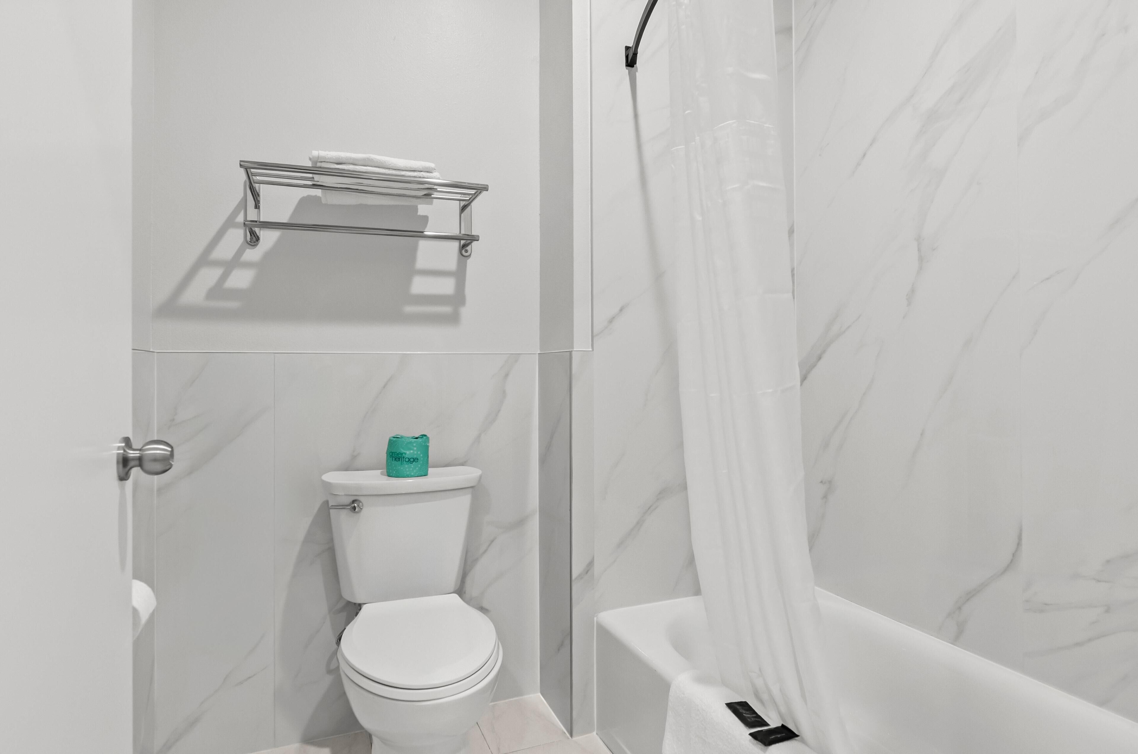 Un baño con inodoro, ducha con cortina transparente y toallero.