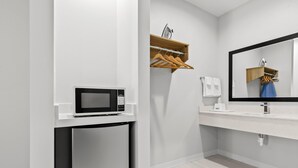 A modern bathroom with a white sink, a mirror, a microwave, and a small refrigerator. - Americas Best Value Inn & Suites Tomball Grand Parkway (Tomball)
