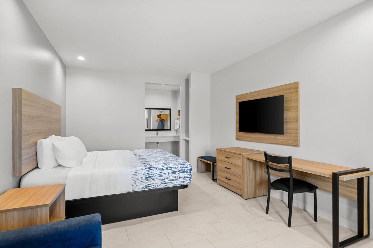 Une chambre d’hôtel moderne équipée d’un lit, d’un bureau, d’une chaise, d’une télévision et d’étagères intégrées.