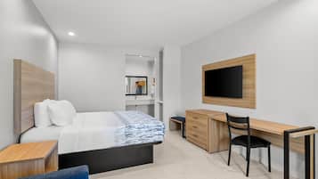 Habitación de hotel moderna con cama, escritorio, silla, televisor y estanterías empotradas.