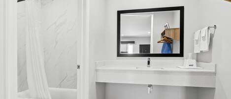 Une salle de bain avec un mur en marbre blanc, une baignoire avec un rideau de douche, un lavabo avec un miroir et un porte-serviettes.