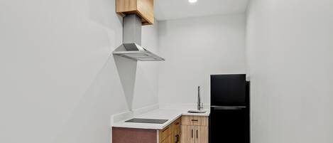 A compact kitchen with a black refrigerator, wooden cabinets, a stainless steel range hood, and a white countertop.