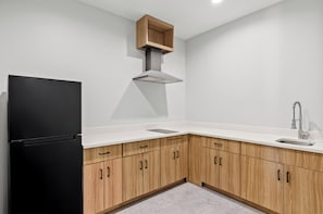 Una cocina moderna con encimeras blancas, armarios de madera, un refrigerador negro y un lavamanos de acero inoxidable.
