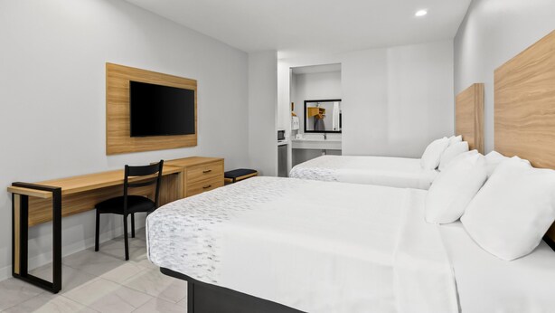 A modern hotel room with two beds, a desk, a chair, a TV mounted on the wall, and a mirror. - Americas Best Value Inn & Suites Tomball Grand Parkway (Tomball)