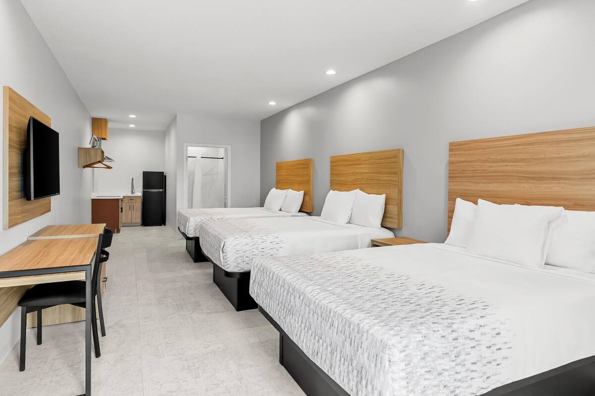 Une chambre d’hôtel avec trois lits, un bureau, une chaise, une télévision et une kitchenette.