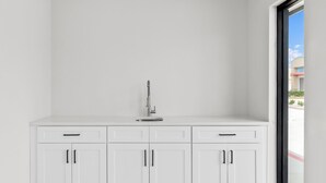 A white kitchen with a modern faucet, three cabinets, and a window with a view of buildings. - Americas Best Value Inn & Suites Tomball Grand Parkway (Tomball)