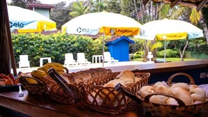 A buffet table with baskets of bread and bananas, and umbrellas with logos. - Chalé do Mar I (São Francisco do Sul)