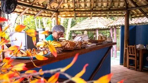 A covered outdoor area with a counter displaying food items, a fan, and a person in the background. - Chalé do Mar I (São Francisco do Sul)