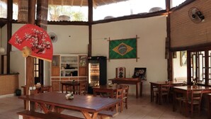 A spacious dining area with wooden tables and benches, a fan, and a Brazilian flag on the wall. - Chalé do Mar I (São Francisco do Sul)