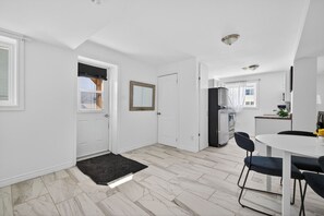 A modern kitchen with white cabinets, a black refrigerator, and a dining area with a white table and black chairs. - Charming Apartment by Aylmer Marina (Gatineau)