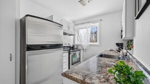 Eine moderne Küche mit Edelstahl-Kühlschrank, Backofen, einer Arbeitsplatte aus Granit und einem Fenster mit transparenten Vorhängen.