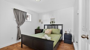 Ein Schlafzimmer mit Bett, Nachttischen, einem Heizkörper und einem Fenster mit Vorhängen.
