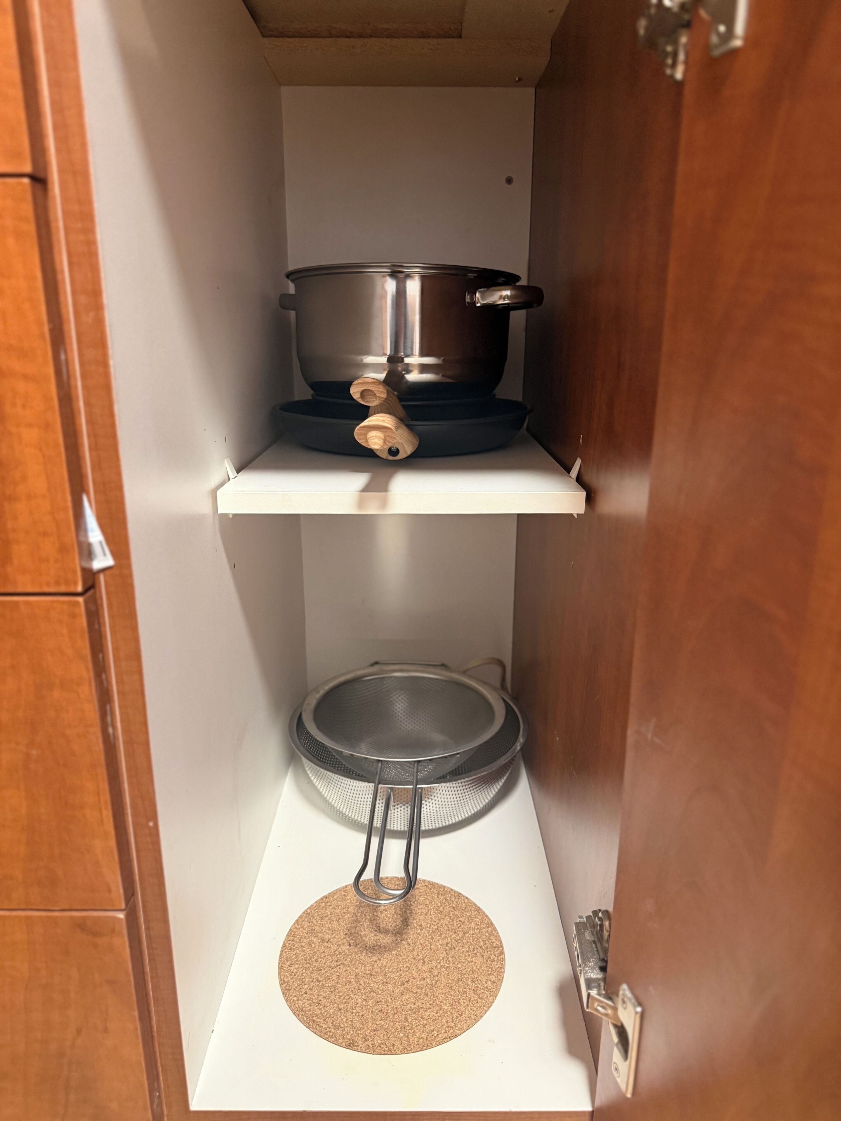 Une cuisine avec une casserole sur la cuisinière, une passoire sur le plan de travail et un meuble en bois.