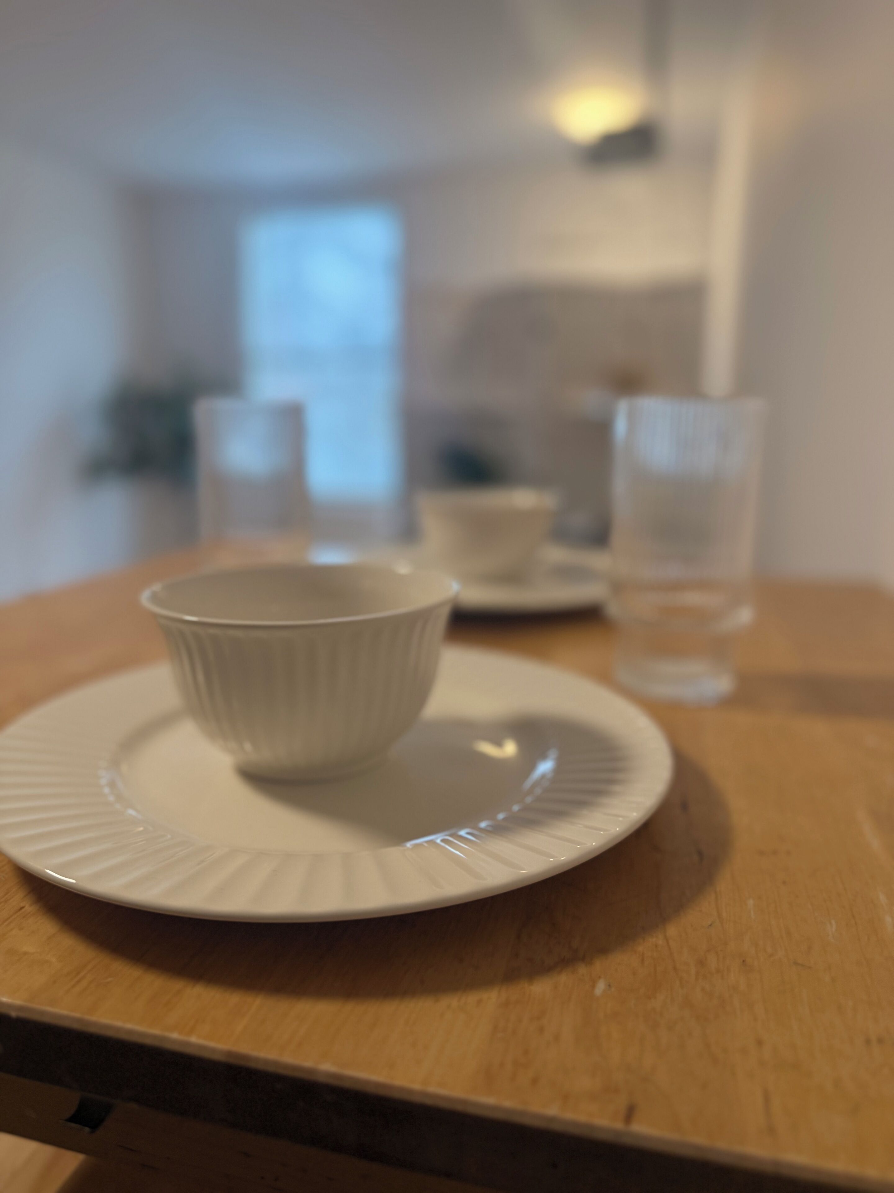 A white ceramic cup on a plate on a wooden table.