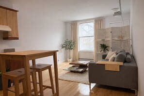 A modern living room with a wooden dining table, a grey sofa, and a glass coffee table.