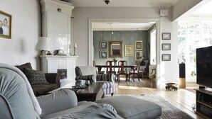 A living room with a grey sofa, a coffee table, and a TV stand. There is a dining area with a table and chairs in the background.
