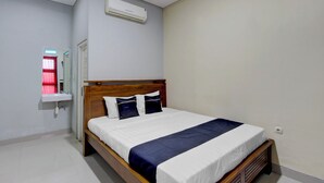 A bedroom with a wooden bed, white bedding, a bedside table, a mirror, and a wall-mounted air conditioner. - Hotel O House Of Fosil Syariah (Semarang)