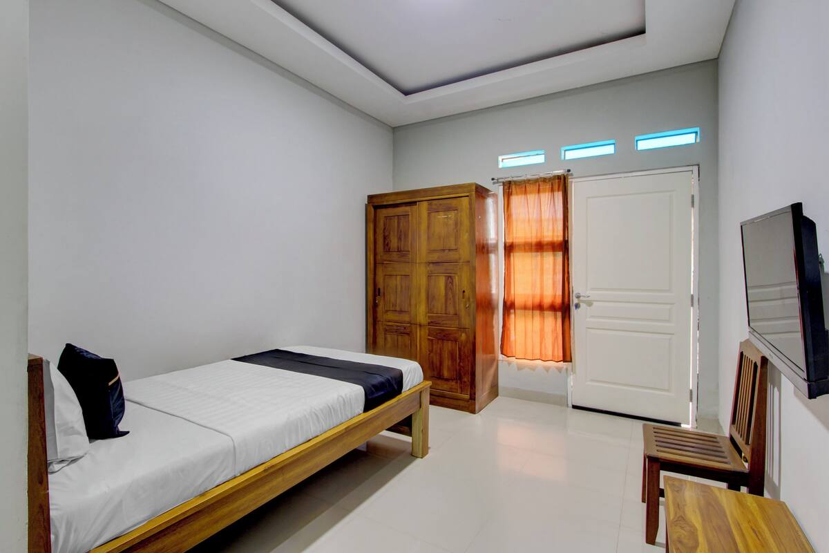 A bedroom with a bed, wooden wardrobe, a door, a small table, and a TV mounted on the wall.