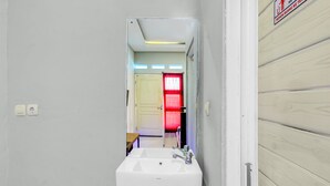 A bathroom with a white sink, a mirror, and a door leading to another room. - Hotel O House Of Fosil Syariah (Semarang)