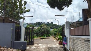 A gated entrance with a sign for the Bank of Public Services, a paved pathway, and a residential area with houses and trees in the background. - Hotel O House Of Fosil Syariah (Semarang)