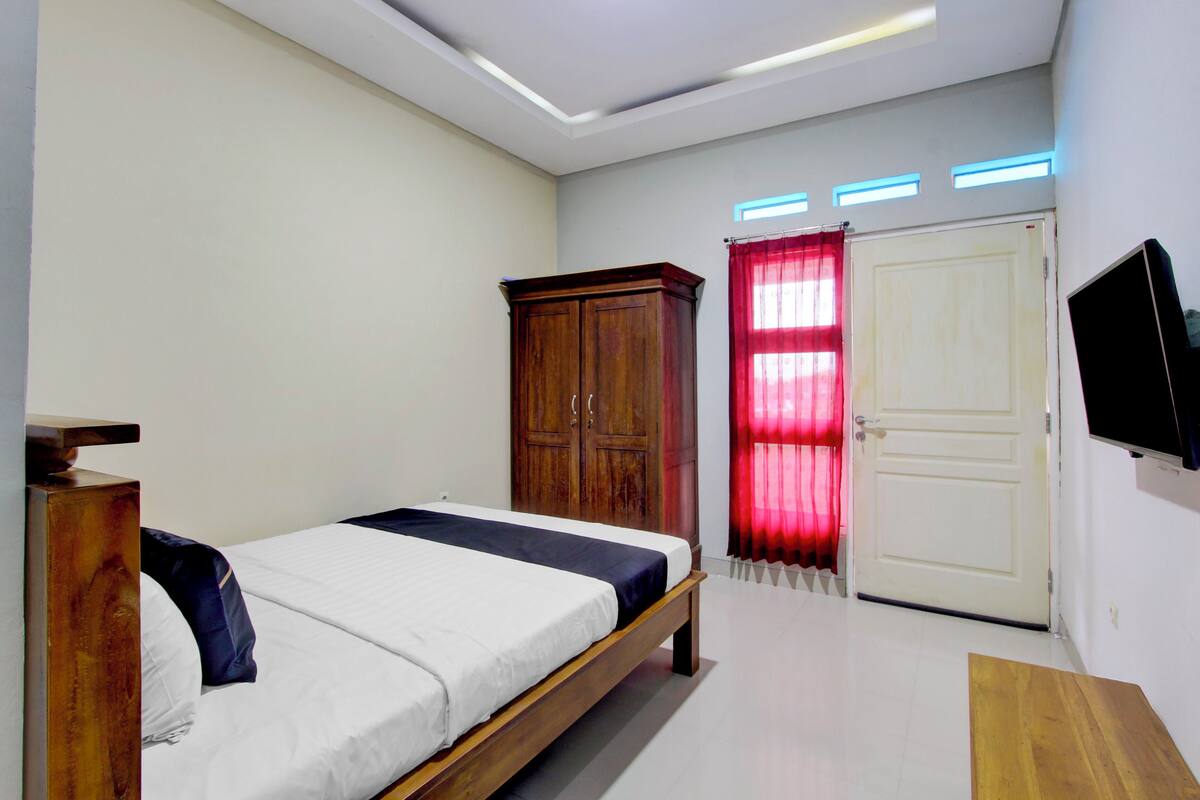 A bedroom with a bed, wooden wardrobe, a door, and a television.
