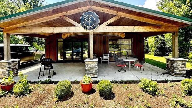 A covered outdoor seating area with a logo, stone pillars, and a grill. - Huron Hideaway - Great Indoor & Outdoor Spaces! (Huron)