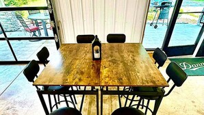 A wooden table with four chairs, a bottle, and a window with a view of greenery. - Huron Hideaway - Great Indoor & Outdoor Spaces! (Huron)