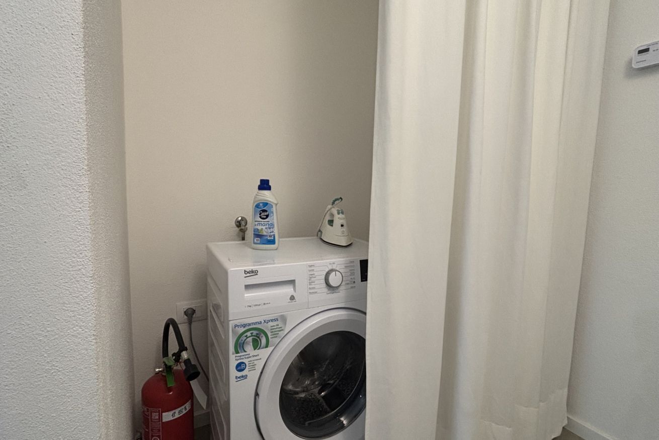 A compact laundry area with a washing machine, a bottle of detergent, and a fire extinguisher.