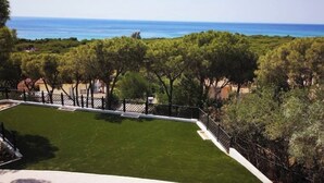 A view of a well-maintained lawn with a fence, trees, and a distant view of the sea. - Levante Apartment - Style and Elegance 300 meters from the sea (Santa Margherita di Pula)