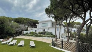 A modern house with a white exterior, a well-maintained lawn, and several white lounge chairs. - Levante Apartment - Style and Elegance 300 meters from the sea (Santa Margherita di Pula)