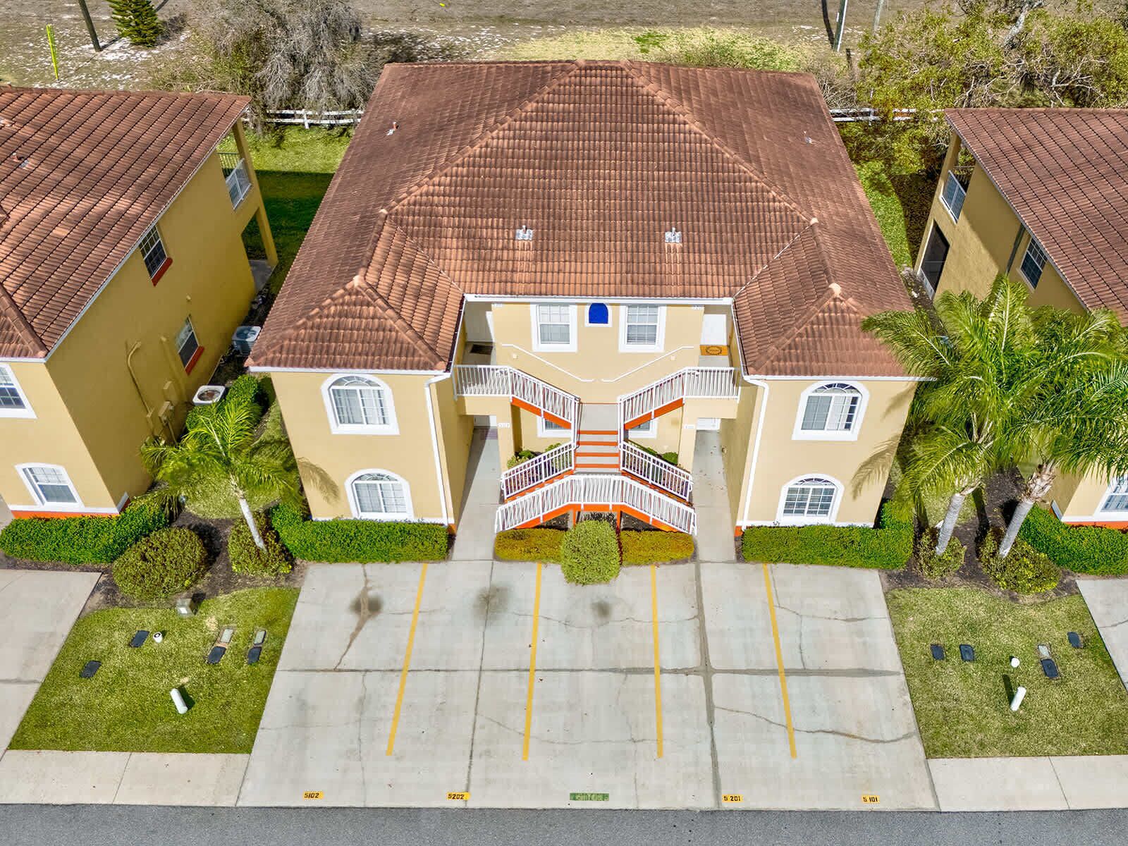 A multi-story building with a central staircase, surrounded by well-maintained lawns and palm trees.