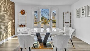 A modern dining room with a marble table, white chairs, and a view through large windows. - Comfortable SFH for Families & Groups • Easy Walk to Local Shops and Eateries (Downers Grove)