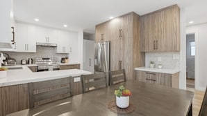 A modern kitchen with white cabinets, a stainless steel refrigerator, and a wooden island with a plant. - Spacious 6BR Full Home Near Niagara Falls & Wine (St. Catharines)