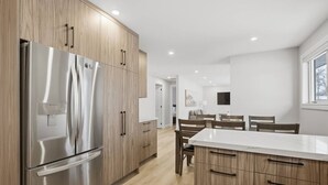 A modern kitchen with stainless steel appliances, wooden cabinets, and a dining area with a white table and chairs. - Spacious 6BR Full Home Near Niagara Falls & Wine (St. Catharines)
