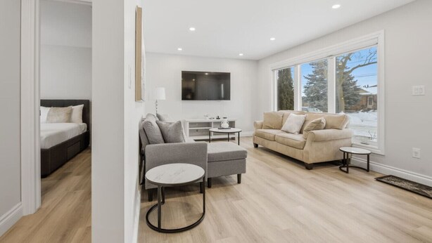 A modern living room with a sofa, armchair, and coffee table. There is a bed in the adjacent room. - Spacious 6BR Full Home Near Niagara Falls & Wine (St. Catharines)