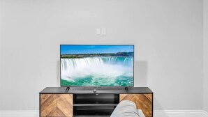 A flat-screen TV mounted on a wall above a wooden TV stand. - Spacious 6BR Full Home Near Niagara Falls & Wine (St. Catharines)