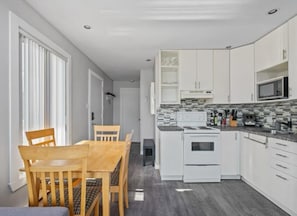 Une cuisine moderne avec des meubles blancs, un four à micro-ondes et une cuisinière. On y trouve également un coin repas avec une table et des chaises en bois.