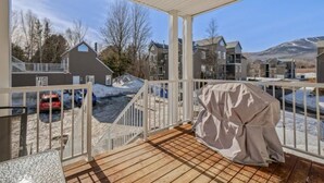 A covered outdoor deck with a grill and a view of a residential area with houses and a snowy landscape. - Condo MSA - Ski Beaupré (Beauprã©)