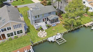 A residential property with a dock, a covered outdoor seating area, and a well-maintained lawn. - Water's Edge Retreat OCMD (Ocean Pines)